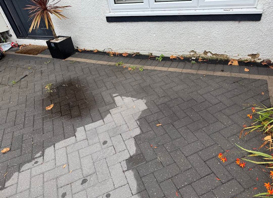 A block-paving driveway being pressure washed by AE Exterior Cleaning, showing a bright clean strip against the ingrained dark grime still to be cleaned.